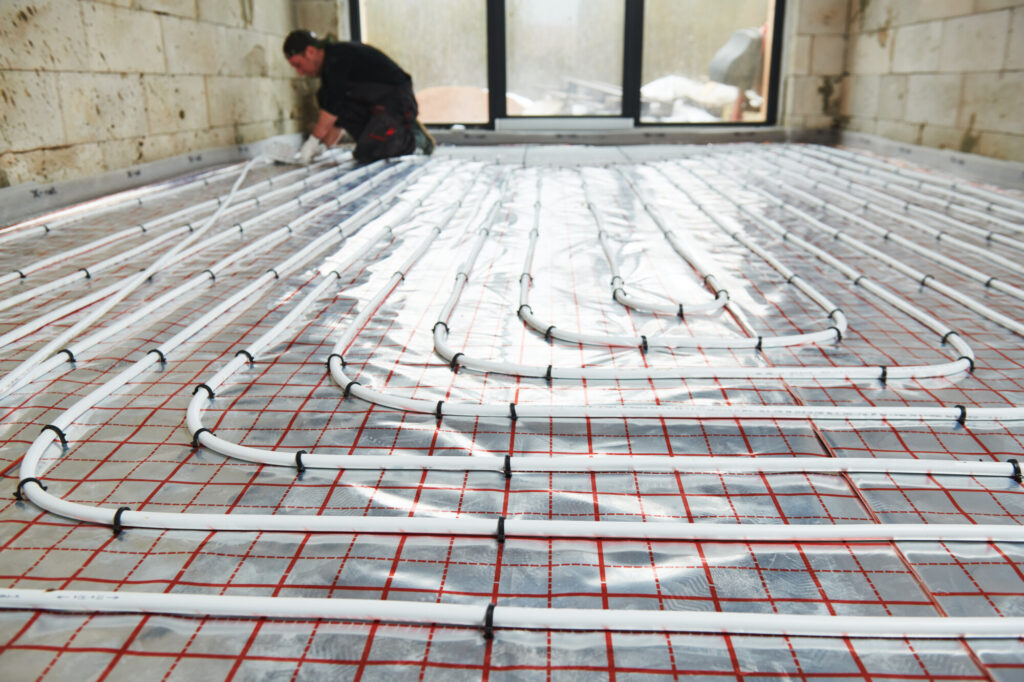Installer fitting underfloor heating pipe loops on insulated floor grid in a residential renovation